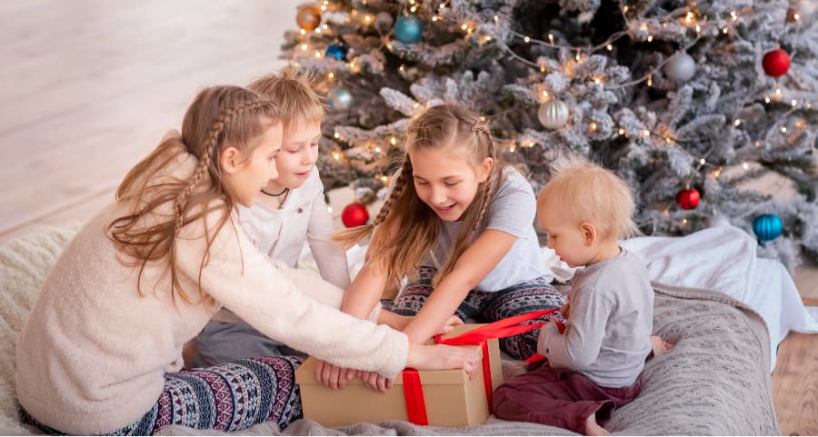 Children opening a gift in the living room beside a Christmas tree.